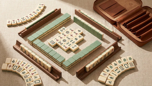A flat-lay of American mahjong tiles arranged beside a wooden rack, tile pusher, and leather carrying case on a warm linen surface, lit by soft natural light.