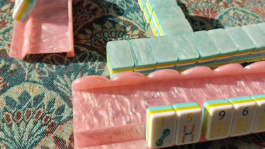 A pink pearlescent mahjong rack displaying BamChive tiles at a game-night table.