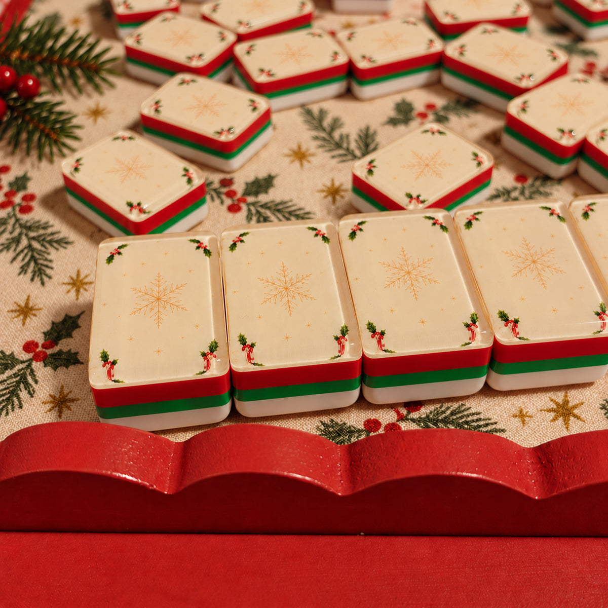 BamChive Cream Christmas Star mahjong tile backs with red, green and white layered edges on a Christmas holly-patterned tablecloth.
